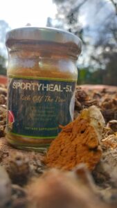 A bottle of Sportyheal-5x with a label, placed on a green background with a field of turmeric plants in the background