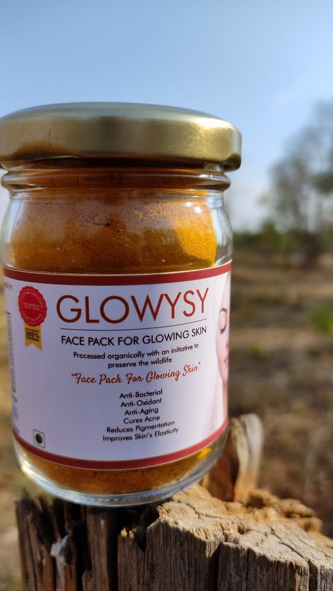 An image of a bottle of Glowysy, a turmeric-based face pack, made from pure turmeric root, hand-cultivated and processed by Bagdara Farms. The bottle has a white label with green text and a green cap, and the product is designed to give your skin a healthy and natural glow.